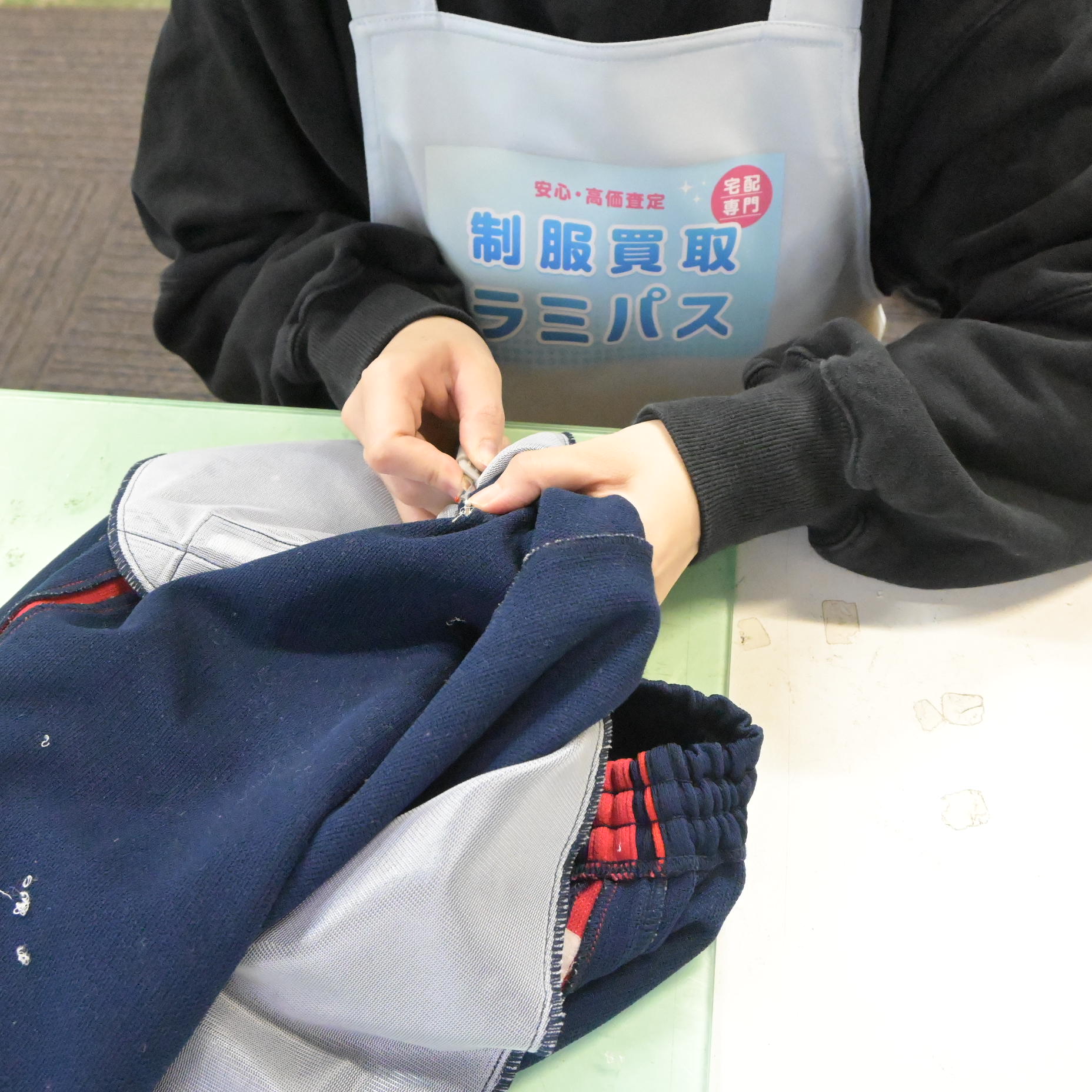 ラミパスのエプロンを着けたスタッフが、リッパーで刺繍除去の繰り返し作業をしている