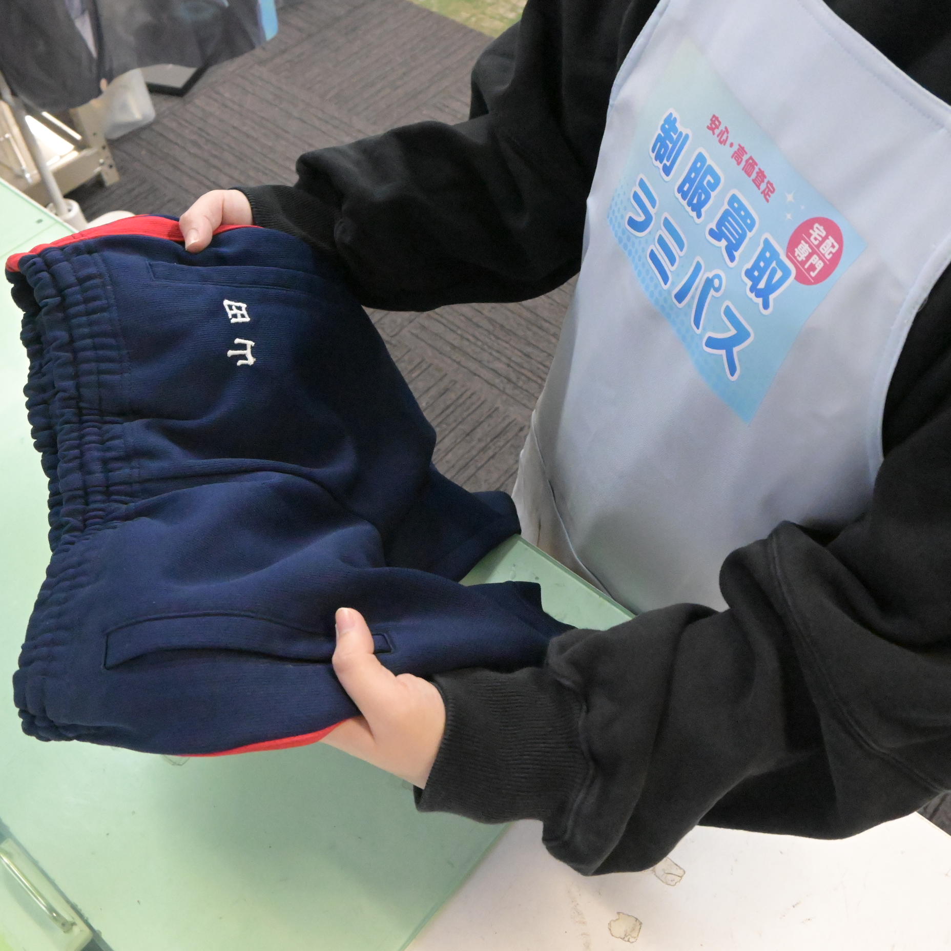 ラミパスのエプロンを着用したスタッフが、作業前に刺繍の位置と状態を確認している