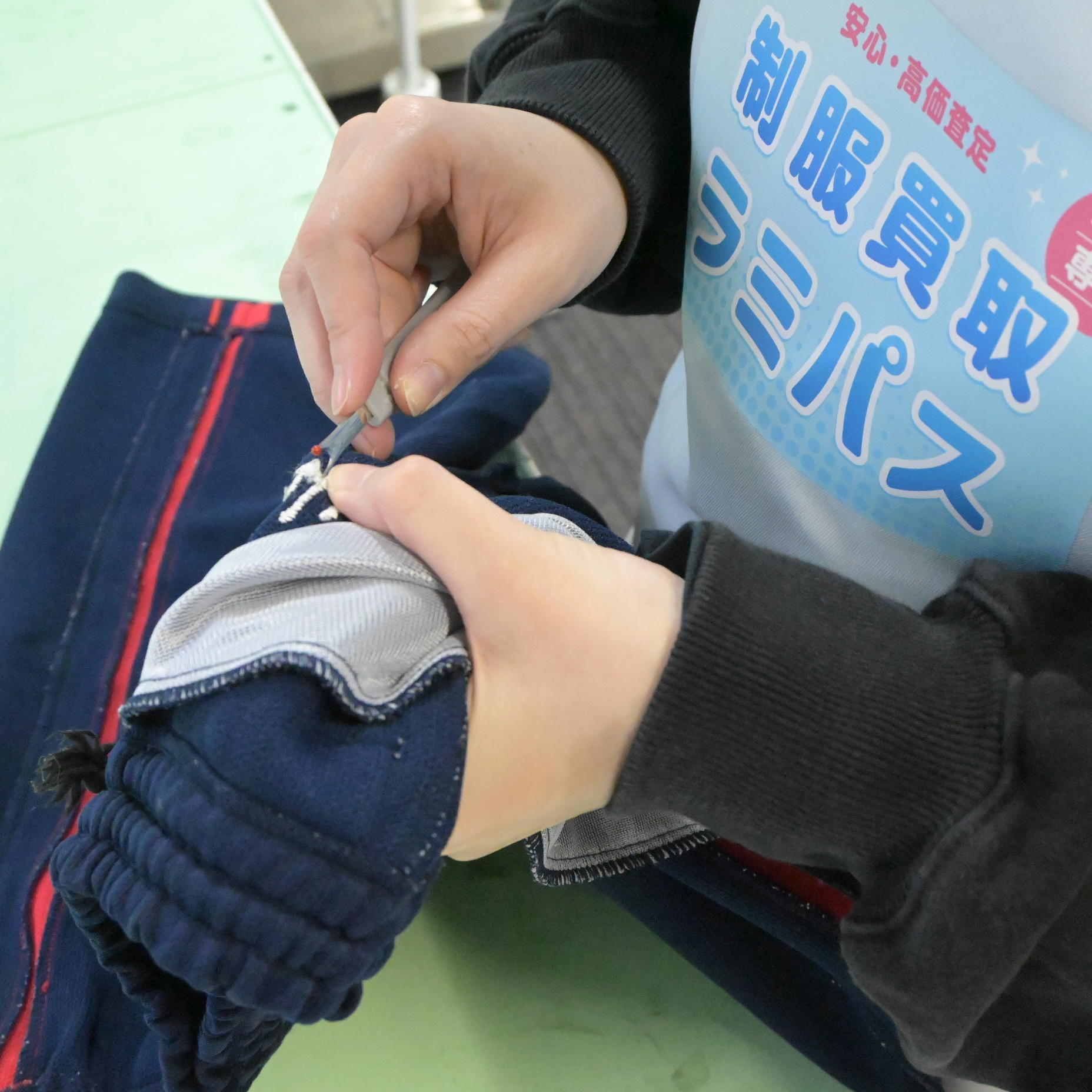 ラミパススタッフがリッパーをジャージの裏側の刺繍糸に当て、少しずつ切っている様子