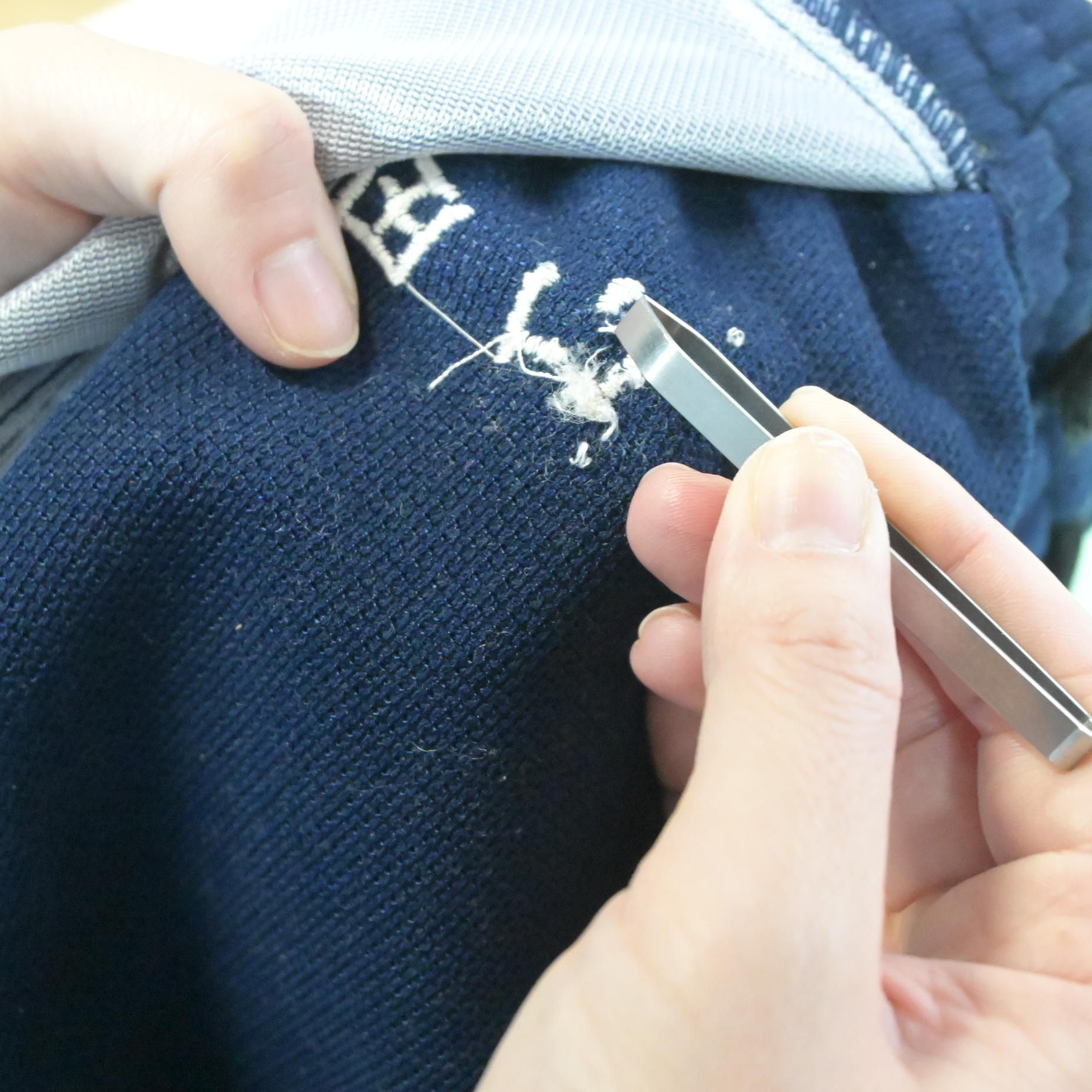 ピンセットで刺繍糸をつまんで引き抜いている作業のアップ。糸がほつれている状態がわかる