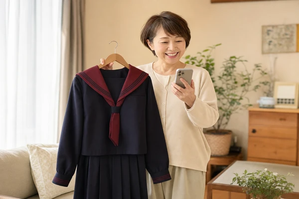 北陸学院の制服をハンガーで持ちスマートフォンで買取相場を確認する母親