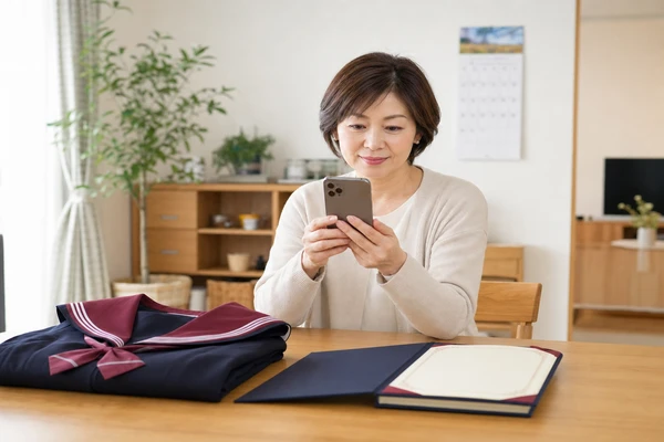 卒業証書と北陸学院制服を前にスマートフォンで買取申し込みをする母親