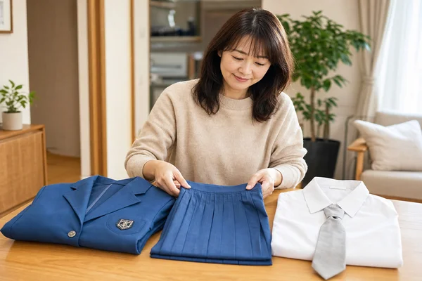 茨城キリスト教学園のブルーのジャケット・スカート・ブラウス・グレーネクタイを丁寧にテーブルに並べて整理するお母さんの写真