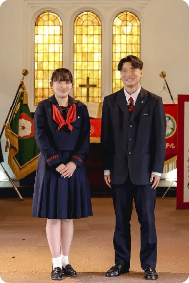 ルーテル学院高等学校の冬服制服。女子は濃紺のセーラー服にえんじ色のネクタイ、男子は濃紺の3つボタンブレザーに赤基調のネクタイを着用している。背景はルーテル学院のチャペル。