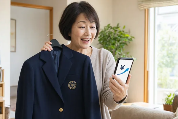 名東高校のネイビーブレザーをハンガーで持ちながらスマートフォンで買取相場を確認して喜ぶお母さんの写真