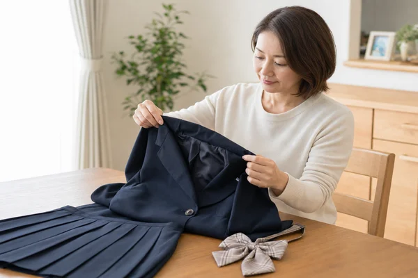 東京家政大学附属女子の紺色制服ジャケットとスカートをテーブルで丁寧に確認する母親