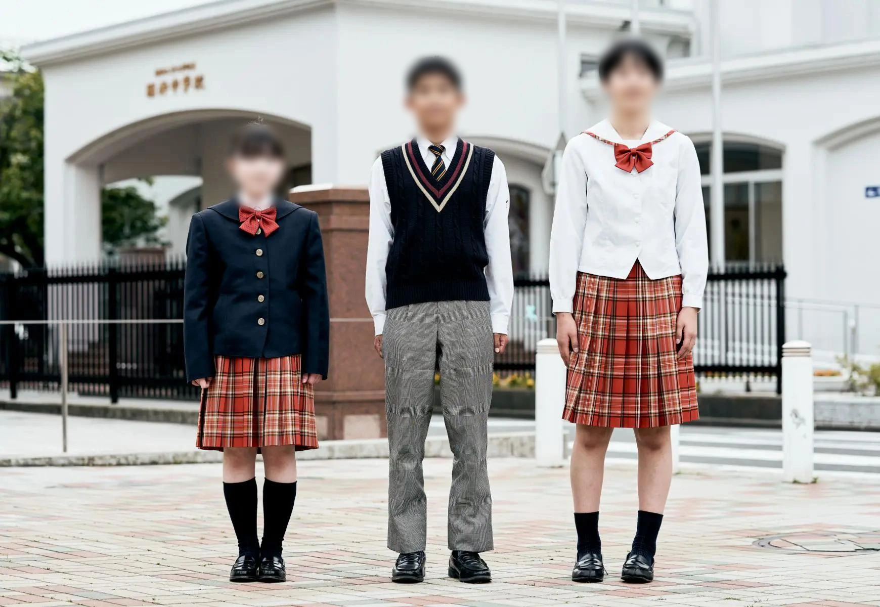 福井工業大学附属福井中学校の制服を着用した3名の生徒。左から冬服の女子（紺ブレザー＋赤チェック柄スカート）、春秋服の男子（紺ニットベスト＋ネクタイ＋グレースラックス）、夏服の女子（白セーラーカラーブラウス＋赤リボン＋赤チェック柄スカート）
