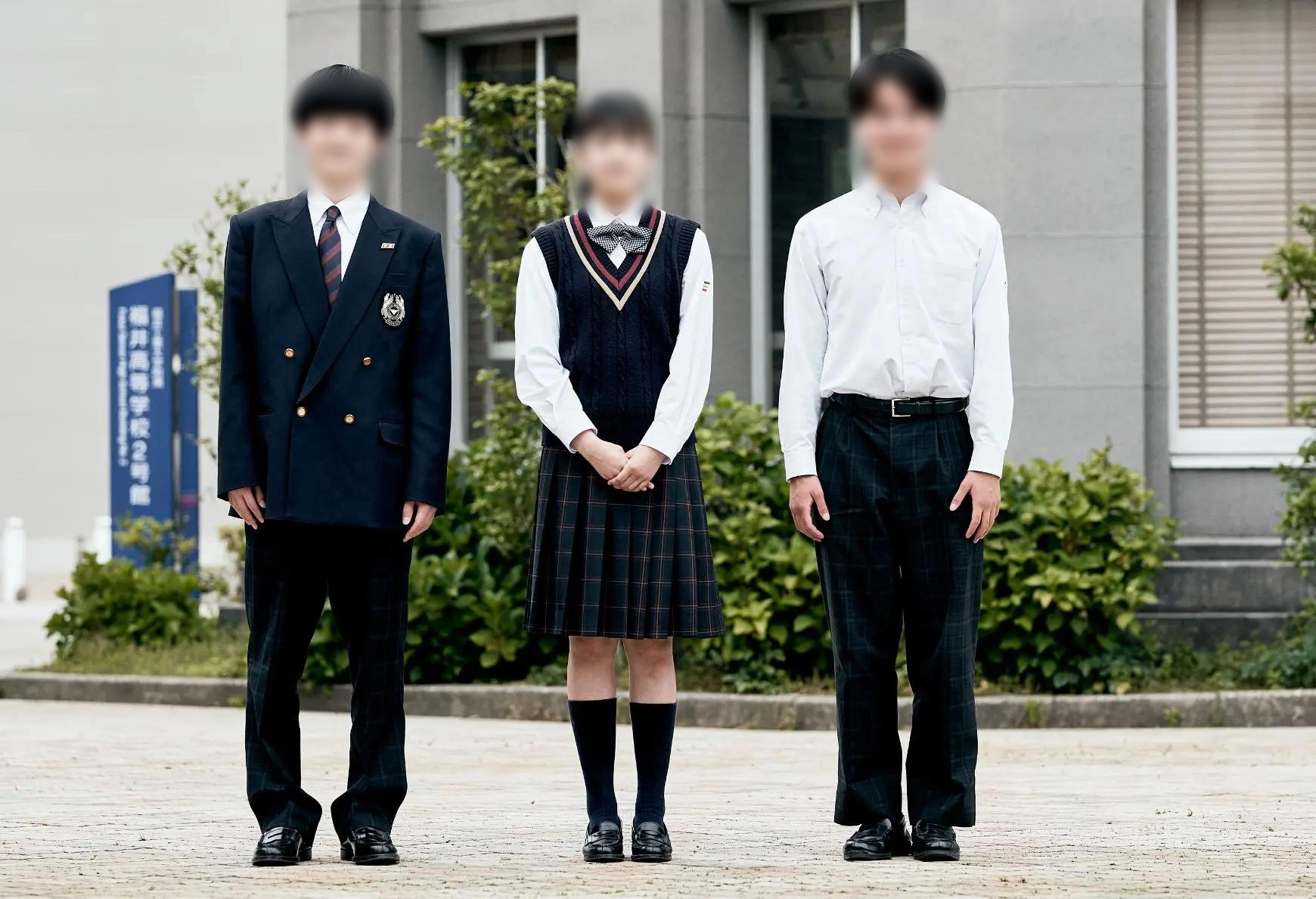 福井工業大学附属福井高等学校の制服を着用した3名の生徒。校舎前で撮影されており、左から冬服の男子（紺ダブルブレザー＋ネクタイ＋紺チェック柄スラックス）、春秋服の女子（紺Vネックニットベスト＋紺チェック柄スカート）、夏服の男子（白長袖シャツ＋紺チェック柄スラックス）