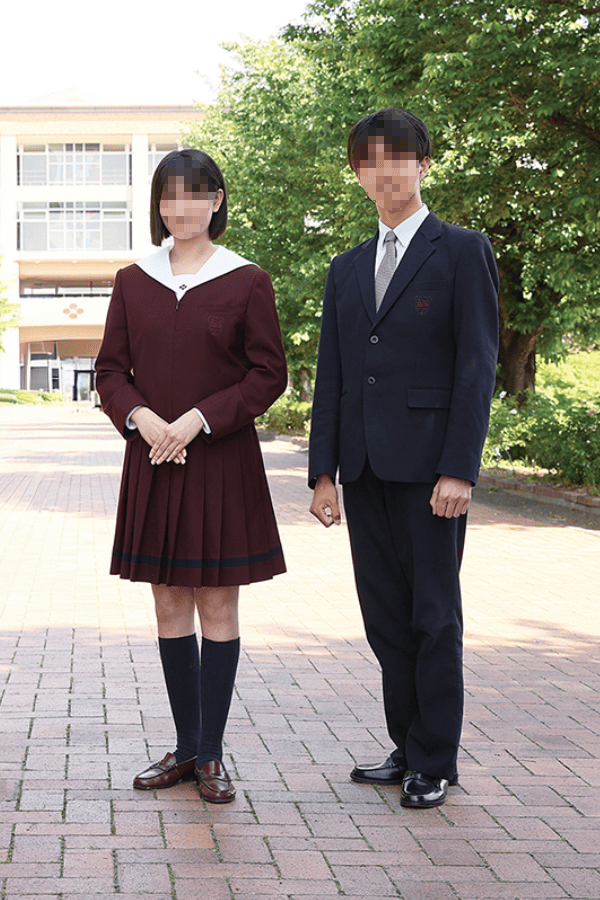 共愛学園高等学校の冬服を着用した男女生徒。女子はボルドーカラーのセーラー上着とプリーツスカート、男子は紺ブレザーとスラックス