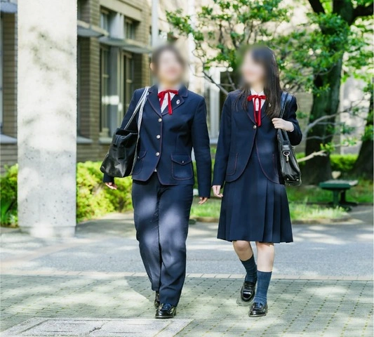 広島女学院中学校の冬服。丸みのあるブレザーにルビーレッドのリボンを合わせ、スラックスとスカートを着用した2人