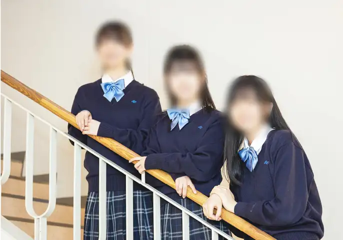 聖カピタニオ女子高等学校の冬服。白ブラウスに紺のVネックセーター、水色のリボン、チェックのプリーツスカートを着用した女子生徒