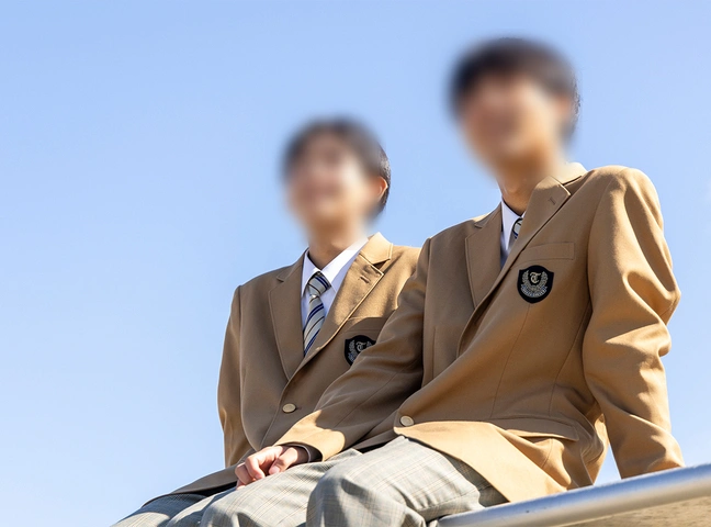 高田高等学校3年制コースの男子冬服。キャメル色のブレザーに校章、ストライプのネクタイ、グレーチェックのスラックスを合わせたスタイル